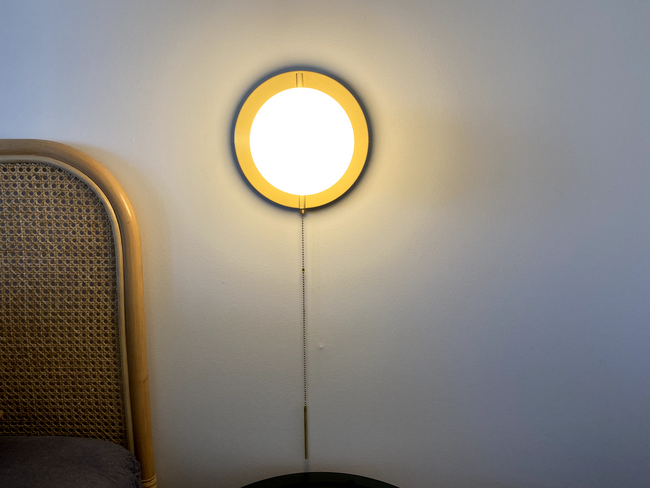 brushed brass round wall lamp with round frosted glass shade, light turned on