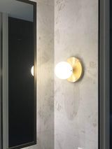 Bathroom concrete wall with brushed brass round wall lamp with round frosted glass shade